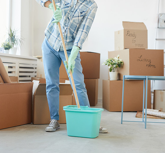 person cleaning with a mop and bucket in a room filled with moving boxes preparing for a new home 3 cleaning tips