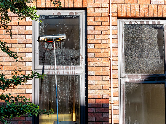 cleaning windows with a squeegee showcasing water streaks and reflection on two glass panes against a brick wall