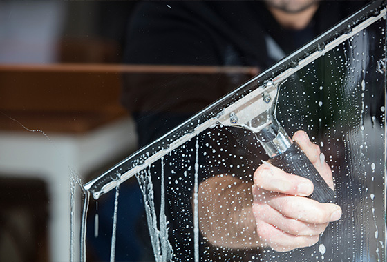 person using a squeegee to clean a window with soap and water for a sparkling finish in three easy steps