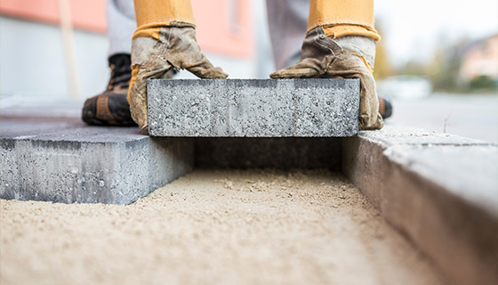 worker placing a concrete block on a sandy base for outdoor construction project involving 4 paving stones