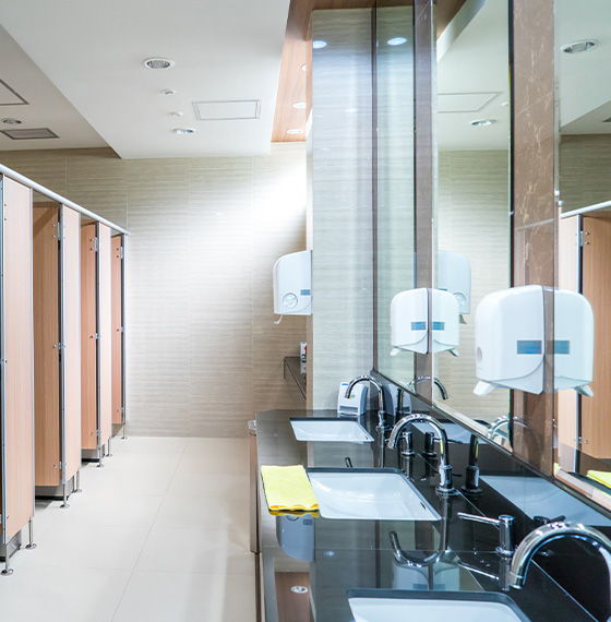 modern public restroom featuring three sinks and stall doors with wooden finish