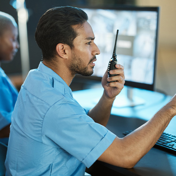 man in blue shirt communicating with radio while monitoring computer screens showing security footage in a control room two way communication