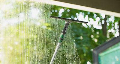 squeegee cleaning a window with raindrops sunlight shining through outside garden view maintaining clear visibility